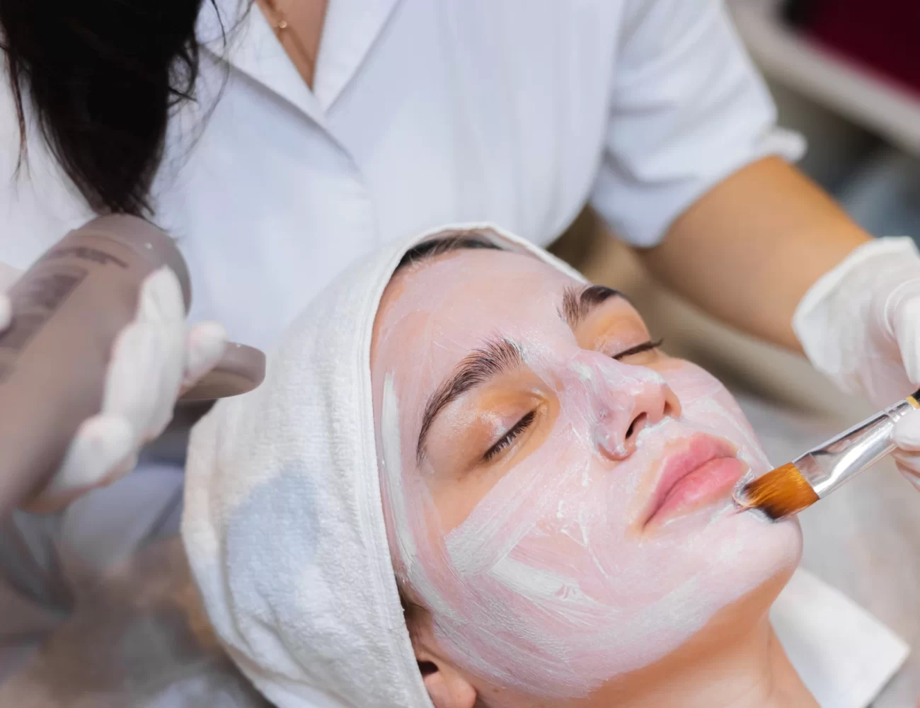 esteticista-con-un-pincel-aplica-una-mascarilla-hidratante-blanca-la-cara-de-un-cliente-joven-en-un-